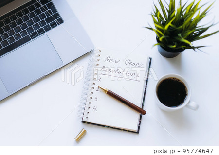 open notepad with new year resolutions and empty list. Flower, laptop and coffee cup on background. open notepad with new year resolutions and empty list. Flower, laptop and coffee cup on background. 95774647