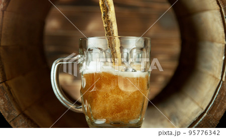 Pouring beer into glass inside old wooden barrel. Pouring beer into glass inside old wooden barrel. 95776342