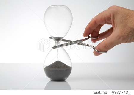hand with scissors near the hourglass. time stop concept. hand with scissors near the hourglass. time stop concept. 95777429