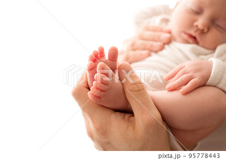 Top view of a newborn girl lying in a white overalls in the arms of her parents. Beautiful portrait of a little girl with closed eyes. The hands of the parents gently hug the child's body. 95778443