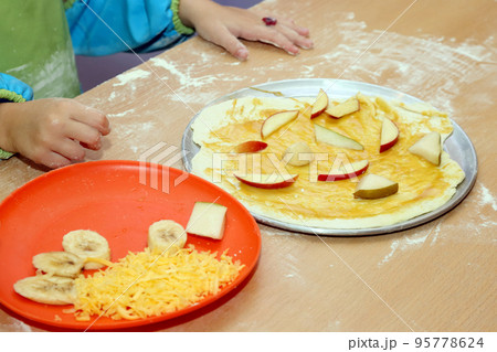 child in uniform preparing fruit pizza closeup 95778624