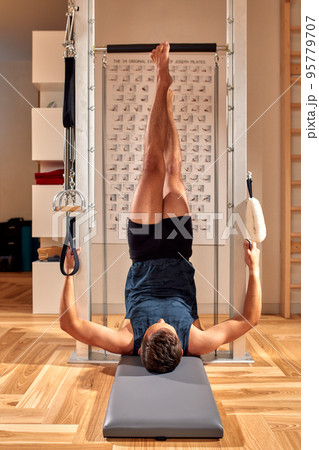 Side view of barefoot male athlete lying on pilates reformer and performing abs exercise during fitness workout. Pilates man concept. 95779707