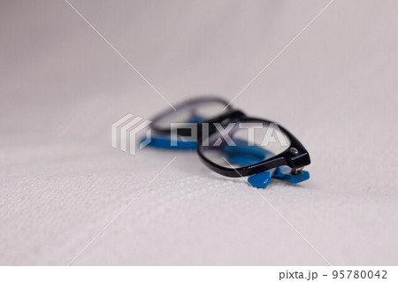 Eyeglasses with a black frame and blue temples close-up on a light background. Eyeglasses with a black frame and blue temples close-up on a light background. 95780042