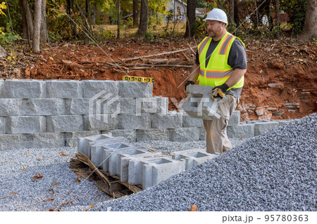 Building retaining wall with retaining blocks on new property is being done by construction worker Building retaining wall with retaining blocks on new property is being done by construction worker 95780363