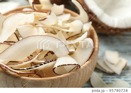 Tasty coconut chips in wooden bowl, closeup Tasty coconut chips in wooden bowl, closeup 95780728