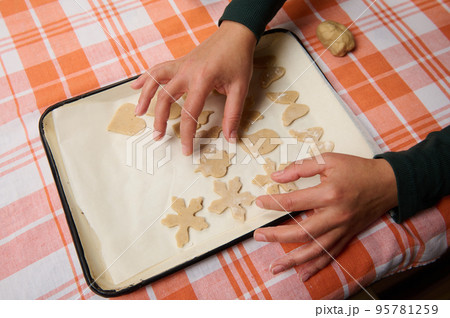 Top view hands of a housewife chef pastry, female confectioner putting cut molds of raw dough on the baking sheet, before placing gingerbread cookies in the hot oven. Christmas culinary and bakery 95781259