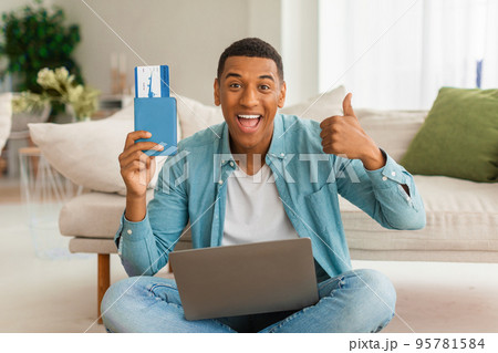 Glad excited millennial african american male with open mouth shows passport and air ticket uses laptop 95781584