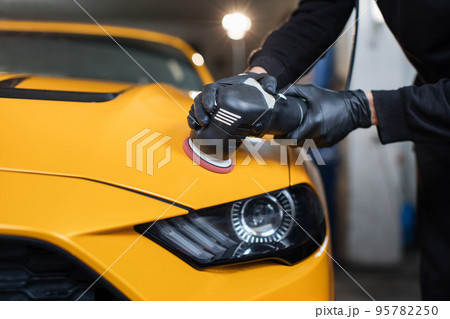 Hands of professional car service worker, with orbital polisher, polishing yellow luxury car hood Hands of professional car service worker, with orbital polisher, polishing yellow luxury car hood 95782250