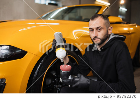 Horizontal shot of man auto service worker, wearing black clothes, putting special polish wax 95782270
