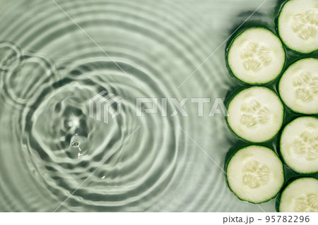 Cucumber slices lie on surface of rippled transparent fresh green water gel with fleck, waves, shadow, expanding circles 95782296