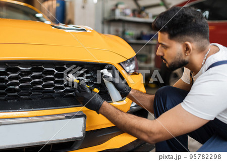 Young bearded male worker in black protective gloves and overalls cleaning radiator grille with foam 95782298