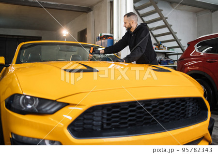 Attractive bearded man in protective glove, applying anti-rain composition for car glass windshield. Attractive bearded man in protective glove, applying anti-rain composition for car glass windshield. 95782343