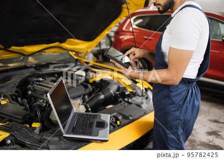 Cropped view of mechanic using tablet computer, recording automobile engine checks 95782425