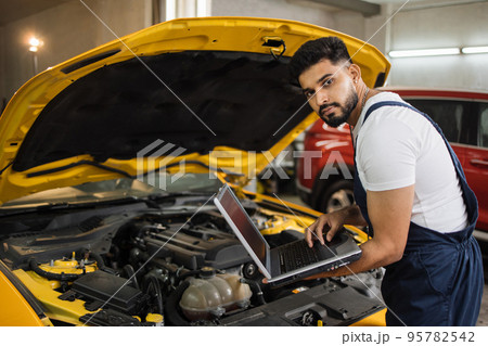 Engineer young man looking at inspection vehicle details under car hood Engineer young man looking at inspection vehicle details under car hood 95782542
