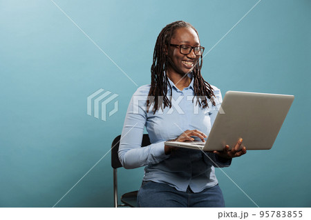 Joyful pretty woman with portable modern computer standing on blue background while surfing web. Excited happy woman having laptop and smiling heartily while browsing webpages on internet 95783855