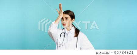Portrait of annoyed, tired woman doctor, facepalm, roll eyes frustrated, bothered by smth stupid, standing in white coat over torquoise background Portrait of annoyed, tired woman doctor, facepalm, roll eyes frustrated, bothered by smth stupid, standing in white coat over torquoise background 95784321