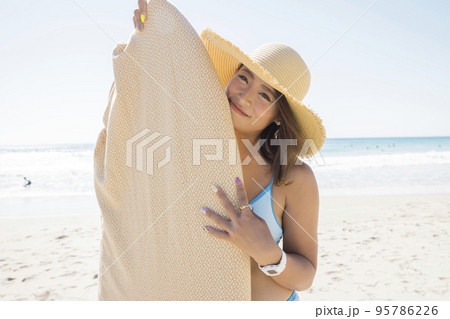 サーフボードを持った麦わら帽子姿の若い女性 95786226