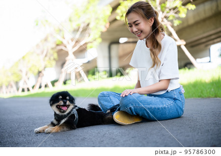 Happy young asian woman playing and sitting on road in the park with her dog. Pet lover concept 95786300