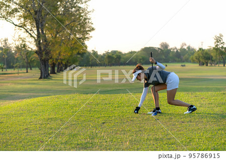 Asian sporty woman putt golf ball on tee off with club in golf course on evening Asian sporty woman putt golf ball on tee off with club in golf course on evening 95786915