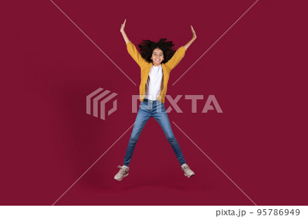 Happy african american kid girl jumping on burgundy background Happy african american kid girl jumping on burgundy background 95786949