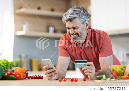 Happy middle aged man buying food online, using cell phone Happy middle aged man buying food online, using cell phone 95787231