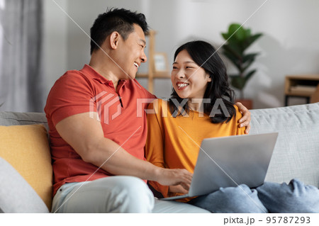 Happy chinese spouses bonding at home, using laptop Happy chinese spouses bonding at home, using laptop 95787293