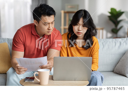 Upset asian couple checking bills, using laptop, home interior 95787465