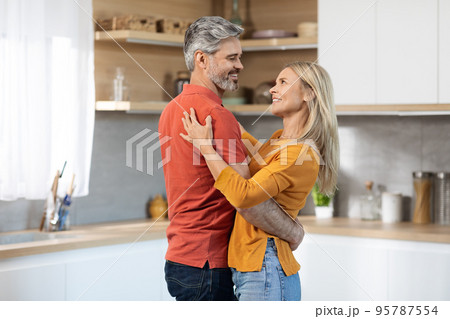 Happily married middle aged couple dancing at kitchen Happily married middle aged couple dancing at kitchen 95787554
