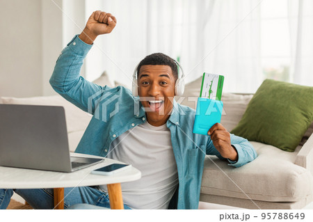 Glad inspired millennial african american guy with laptop shows passport, air ticket and rejoices in trip Glad inspired millennial african american guy with laptop shows passport, air ticket and rejoices in trip 95788649