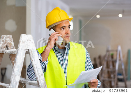 Young foreman with documents in his hands is talking on a mobile phone 95788961