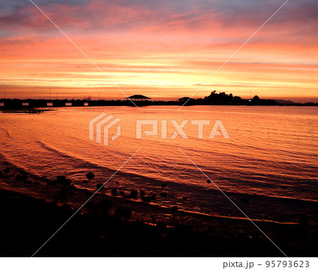 Dramatic sky and reflection at sea surface with silhouette of bridge and island 95793623