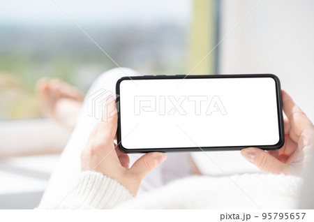 mockup cellphone. Woman lies in relaxed position and watches video content on cellphone or mobile smartphone with white blank screen. holding phone horizontally mockup cellphone. Woman lies in relaxed position and watches video content on cellphone or mobile smartphone with white blank screen. holding phone horizontally 95795657