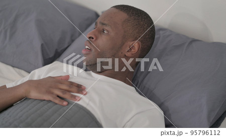 African Man Waking up from Nightmare in Bed 95796112