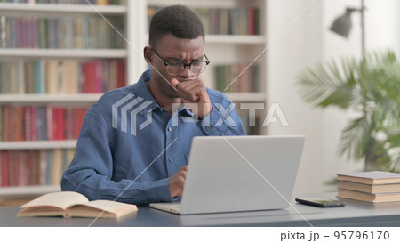 Young African Man Coughing while using Laptop in Office Young African Man Coughing while using Laptop in Office 95796170