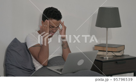 African Woman having Headache while Working on Laptop in Bed 95796539