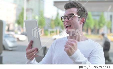Young Man Celebrating Success on Tablet Outdoor 95797734