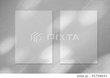 Two empty white vertical rectangle poster mockup with diagonal window shadow on the wall 95798643