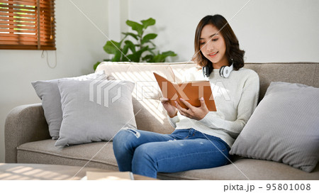 Gorgeous young Asian woman reading a book or novel while relaxing in her living room Gorgeous young Asian woman reading a book or novel while relaxing in her living room 95801008