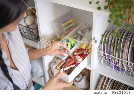 Female tailor choosing thread color for sewing clothes arrangement at box storage cupboard closeup Female tailor choosing thread color for sewing clothes arrangement at box storage cupboard closeup 95801913