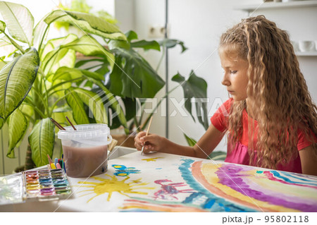 Laughing blonde curly little girl drawing paper art picture chalks sitting on near childish hovel 95802118
