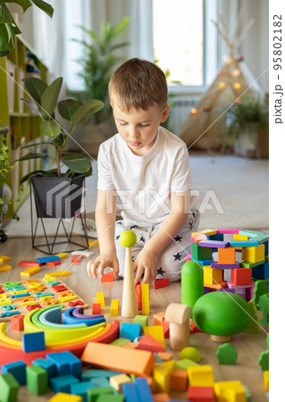 Confident male kid building fortress tower architecture and forest with trees wooden bricks ecology Montessori material Confident male kid building fortress tower architecture and forest with trees wooden bricks ecology Montessori material 95802182