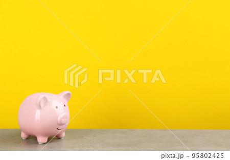 Pink piggy bank on light grey table against yellow background. Space for text Pink piggy bank on light grey table against yellow background. Space for text 95802425