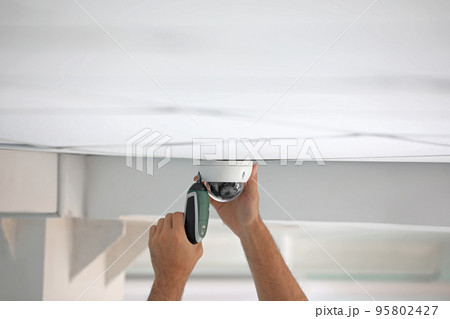 Technician installing CCTV camera on ceiling indoors, closeup Technician installing CCTV camera on ceiling indoors, closeup 95802427