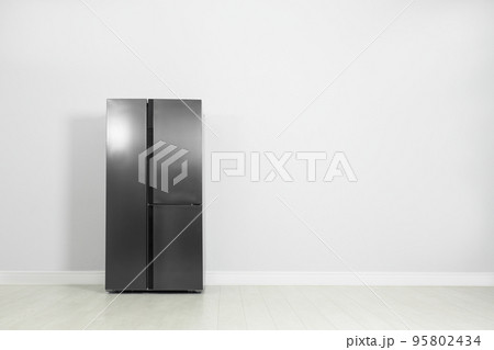 Modern refrigerator near light grey wall, space for text 95802434