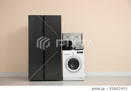 Modern refrigerator and other household appliances near beige wall indoors 95802451