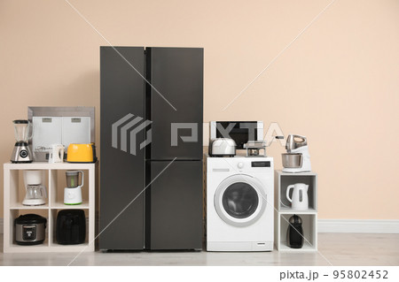 Modern refrigerator and other household appliances near beige wall indoors Modern refrigerator and other household appliances near beige wall indoors 95802452