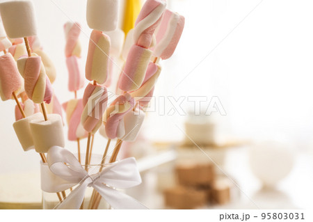 Tasty marshmallow on wooden sticks with bow in room decorated for birthday party, closeup 95803031