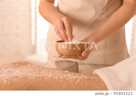 Young woman having body scrubbing procedure with sea salt in spa salon, closeup Young woman having body scrubbing procedure with sea salt in spa salon, closeup 95803323