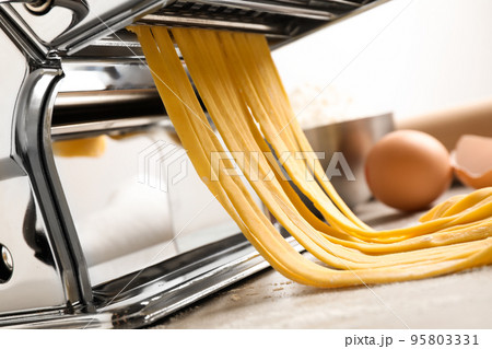 Pasta maker machine with dough on grey table, closeup Pasta maker machine with dough on grey table, closeup 95803331