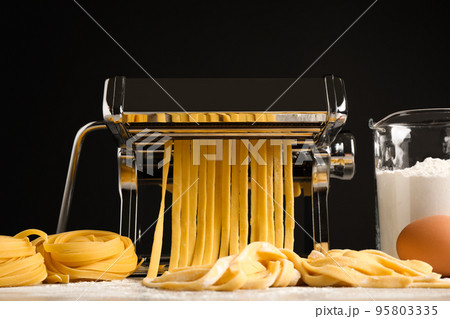 Pasta maker machine with dough and products on grey table against black background Pasta maker machine with dough and products on grey table against black background 95803335
